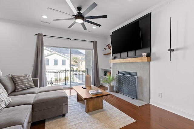 living room featuring visible vents, a fireplace with flush hearth, ornamental molding, wood finished floors, and a ceiling fan