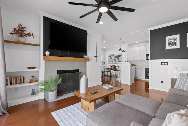 living area with wood finished floors, a large fireplace, a ceiling fan, and ornamental molding