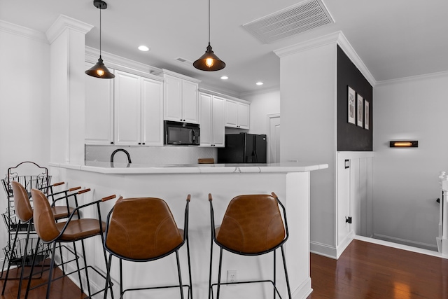 kitchen featuring visible vents, dark wood-type flooring, a kitchen bar, a peninsula, and black appliances