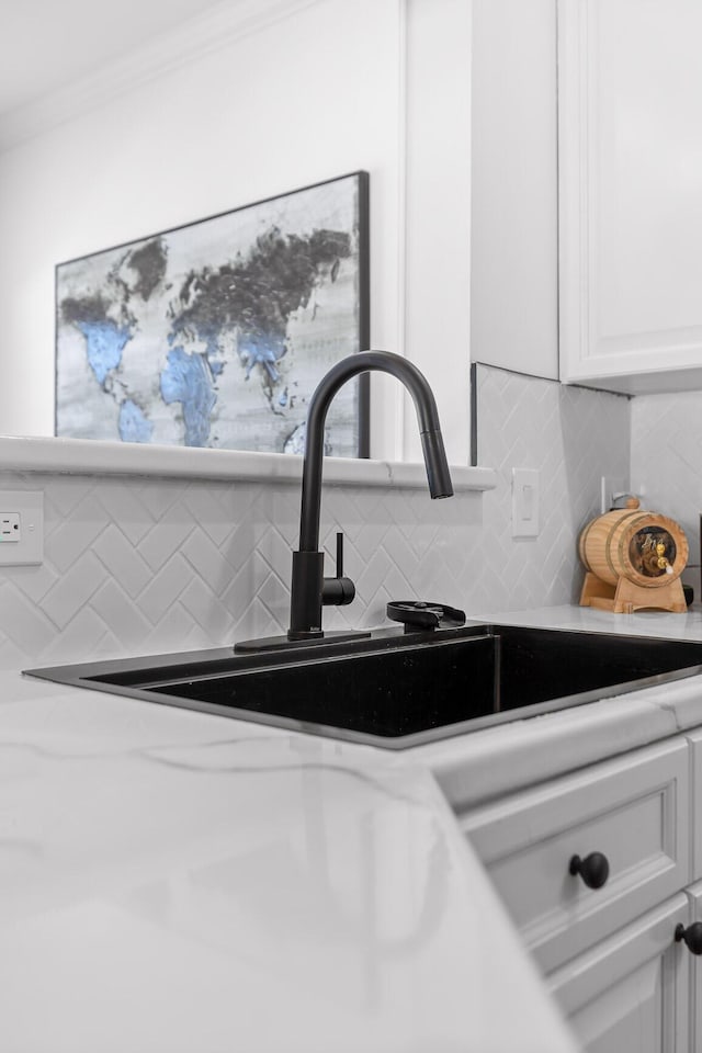 details featuring tasteful backsplash, white cabinets, crown molding, and a sink