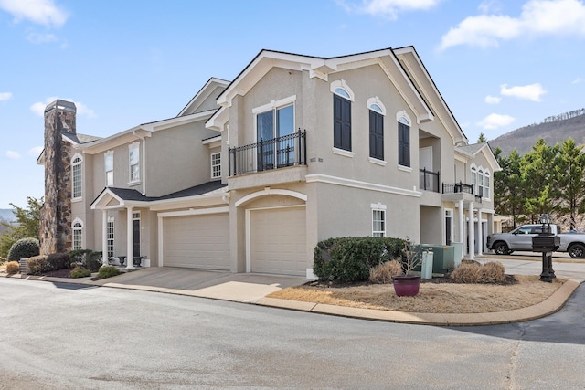 multi unit property with concrete driveway, stucco siding, a chimney, a balcony, and an attached garage