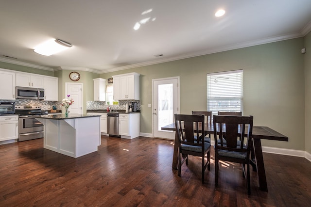 kitchen with dark wood-type flooring, appliances with stainless steel finishes, white cabinetry, dark countertops, and backsplash