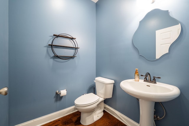 half bathroom with toilet, wood finished floors, and baseboards