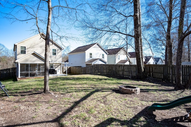 view of yard with a playground, a fenced backyard, a sunroom, and an outdoor fire pit