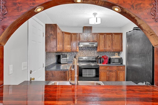 kitchen with arched walkways, stainless steel microwave, a sink, under cabinet range hood, and black / electric stove