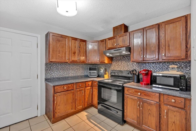 kitchen with light tile patterned floors, black range with electric cooktop, under cabinet range hood, brown cabinets, and stainless steel microwave