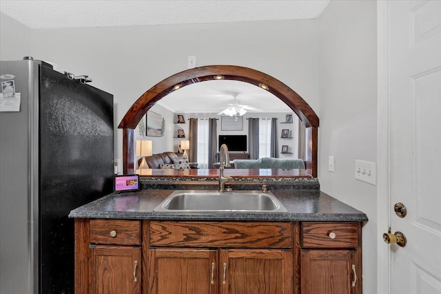 kitchen featuring arched walkways, dark countertops, freestanding refrigerator, open floor plan, and a sink