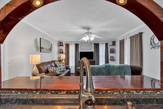 living area with a ceiling fan, ornamental molding, arched walkways, and a textured ceiling