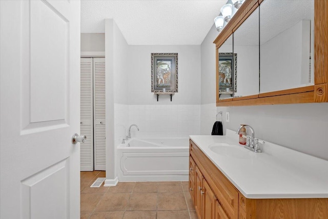 bathroom featuring a textured ceiling, tile patterned flooring, a garden tub, vanity, and a closet