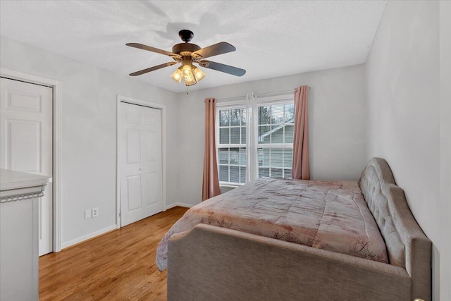 bedroom with ceiling fan, light wood-style flooring, baseboards, and a textured ceiling