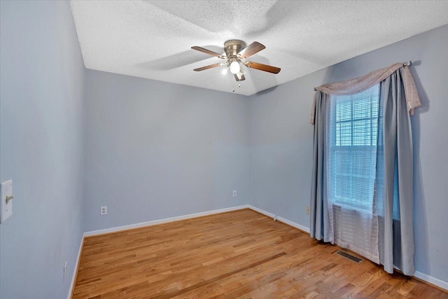 spare room featuring a textured ceiling, wood finished floors, a ceiling fan, visible vents, and baseboards