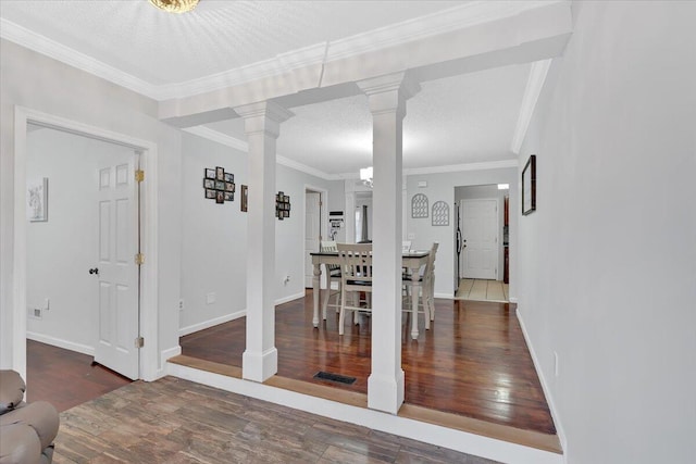 dining area with a textured ceiling, wood finished floors, visible vents, decorative columns, and crown molding