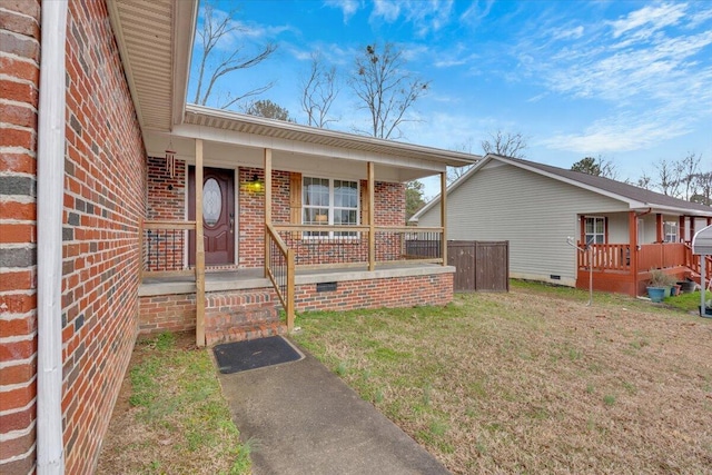 doorway to property featuring crawl space, brick siding, a lawn, and covered porch