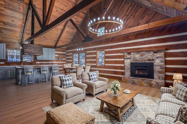 living area with beam ceiling, a notable chandelier, a stone fireplace, wood finished floors, and wooden ceiling