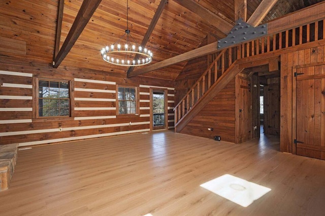 unfurnished living room featuring a notable chandelier, beamed ceiling, stairway, and wooden walls