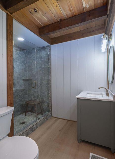 full bathroom with beam ceiling, toilet, a shower stall, wood finished floors, and wooden ceiling