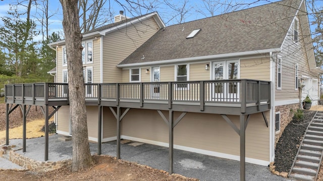 back of property featuring driveway, a shingled roof, a chimney, and a deck