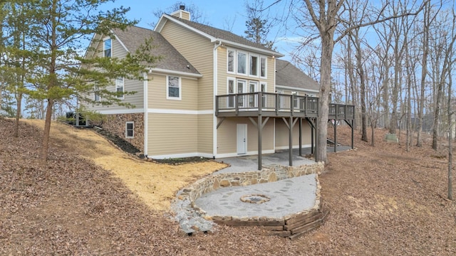 view of side of property featuring a shingled roof, stone siding, a chimney, and a wooden deck