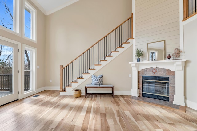 entrance foyer with a tile fireplace, a towering ceiling, baseboards, ornamental molding, and hardwood / wood-style floors