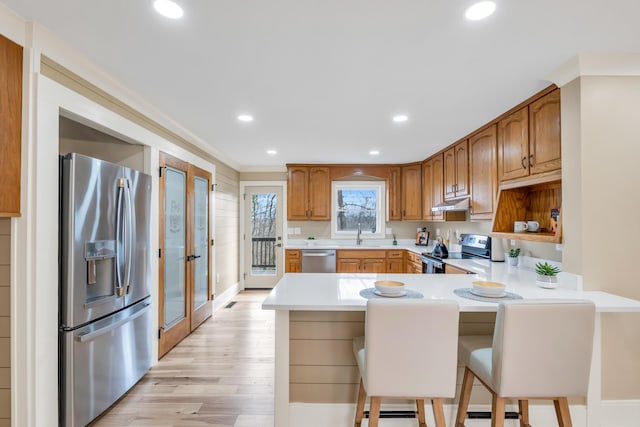 kitchen with stainless steel appliances, light countertops, a peninsula, light wood-type flooring, and under cabinet range hood