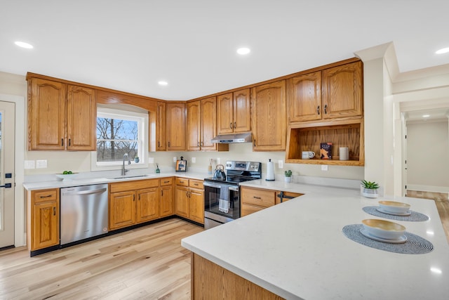 kitchen with appliances with stainless steel finishes, light countertops, a sink, and under cabinet range hood