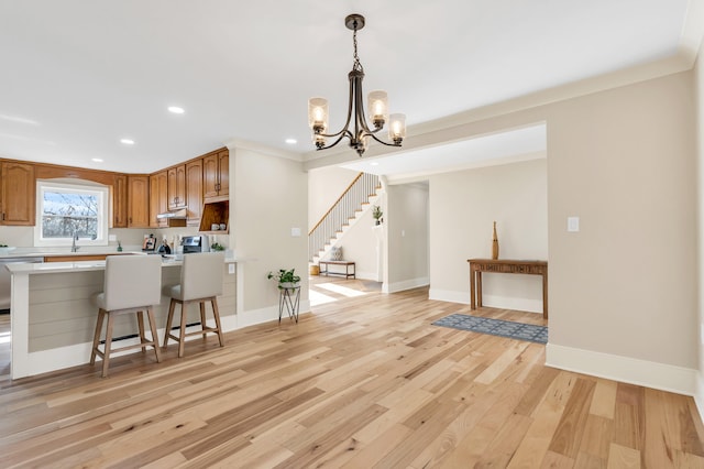 kitchen with pendant lighting, light countertops, light wood-style floors, under cabinet range hood, and baseboards