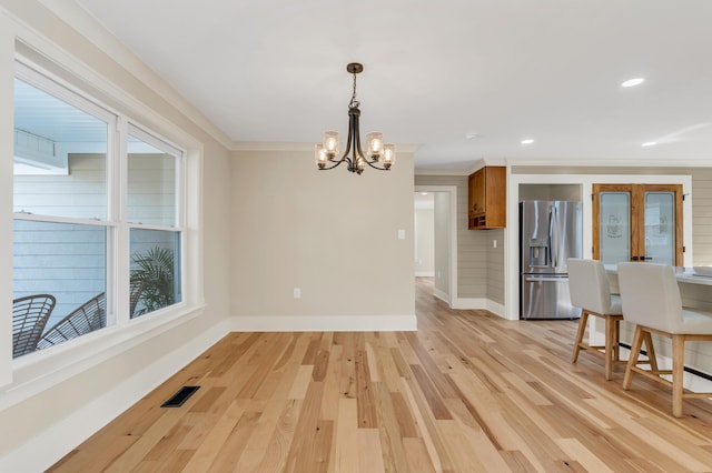 dining space featuring baseboards, visible vents, ornamental molding, an inviting chandelier, and light wood-style floors