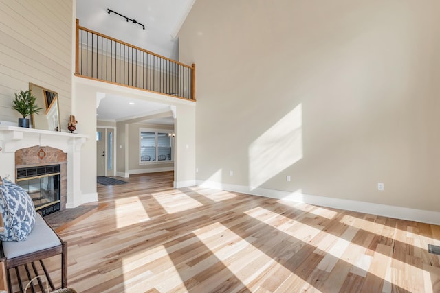 unfurnished living room with track lighting, a tile fireplace, a high ceiling, and wood finished floors