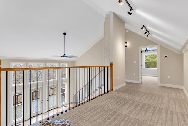 corridor with rail lighting, carpet flooring, vaulted ceiling, and baseboards