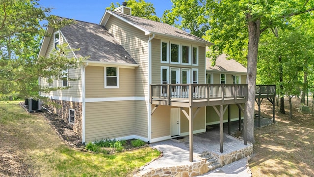 rear view of property with a chimney, roof with shingles, a wooden deck, a patio area, and cooling unit