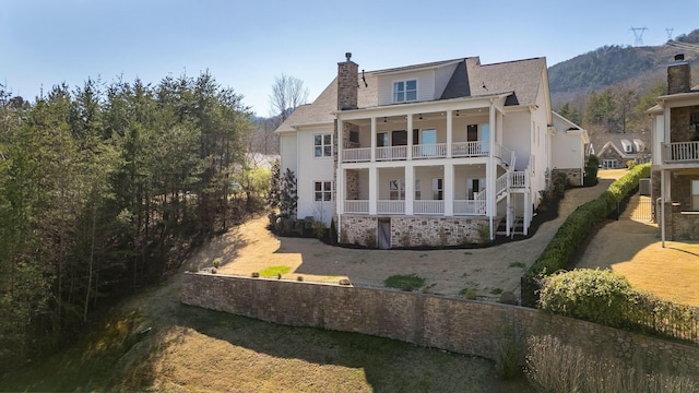 rear view of property with ceiling fan, a porch, a chimney, and a balcony