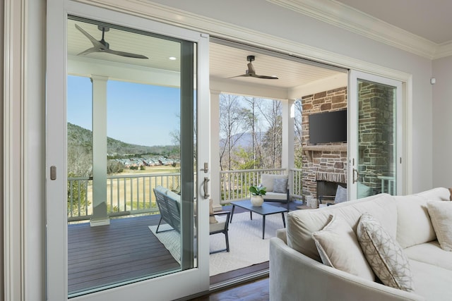 doorway with crown molding, wood finished floors, a ceiling fan, and an outdoor stone fireplace