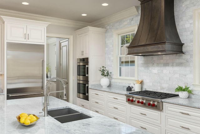 kitchen featuring premium range hood, ornamental molding, a sink, backsplash, and appliances with stainless steel finishes