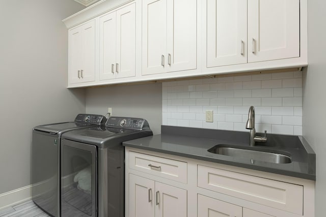 clothes washing area featuring cabinet space, washer and dryer, baseboards, and a sink