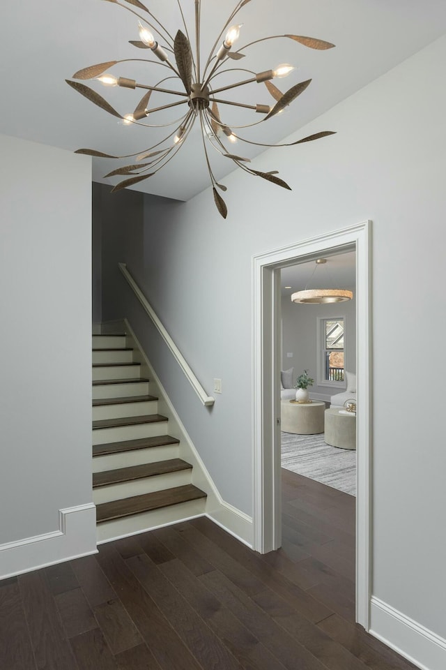 staircase featuring wood finished floors, baseboards, and a chandelier