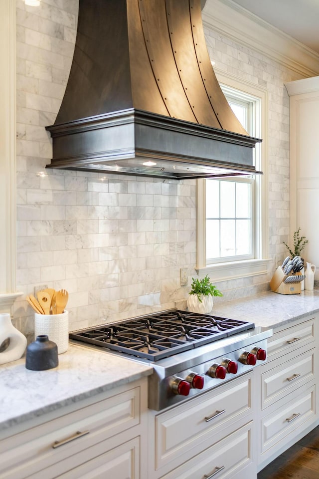 kitchen with light stone countertops, premium range hood, ornamental molding, stainless steel gas stovetop, and tasteful backsplash