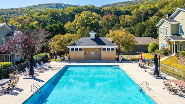 community pool with a patio area, fence, and a view of trees