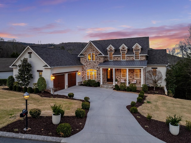 view of front of house with a front yard, driveway, covered porch, a garage, and stone siding