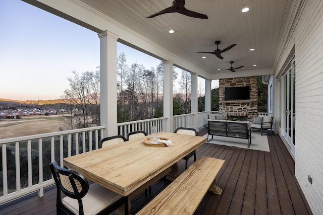 deck at dusk featuring an outdoor living space with a fireplace, outdoor dining space, and a ceiling fan