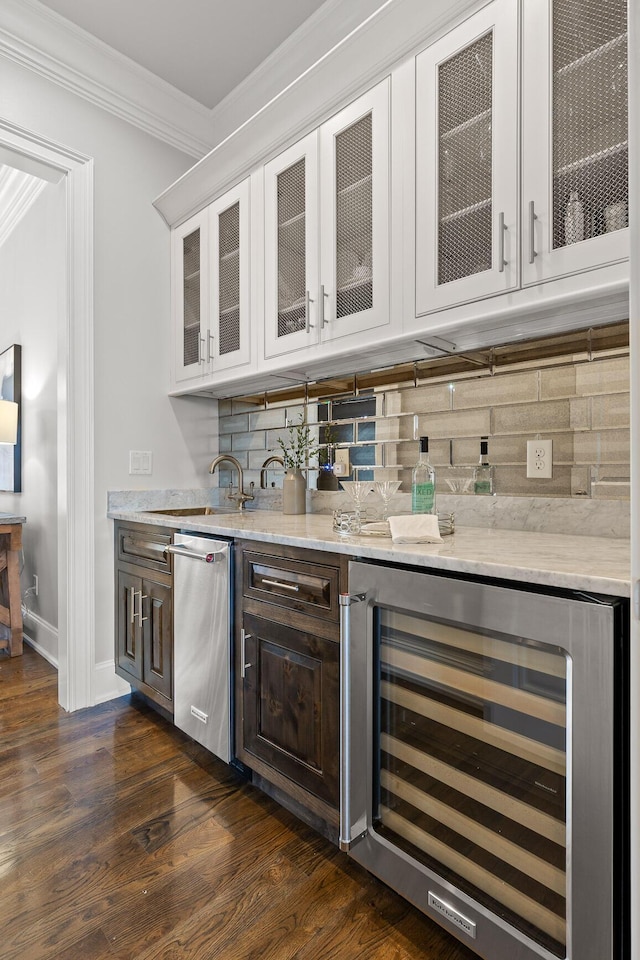 bar featuring tasteful backsplash, beverage cooler, ornamental molding, indoor wet bar, and stainless steel dishwasher