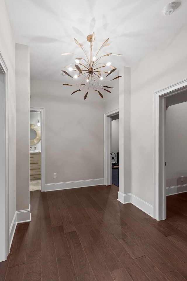 hall with an inviting chandelier, wood finished floors, and baseboards