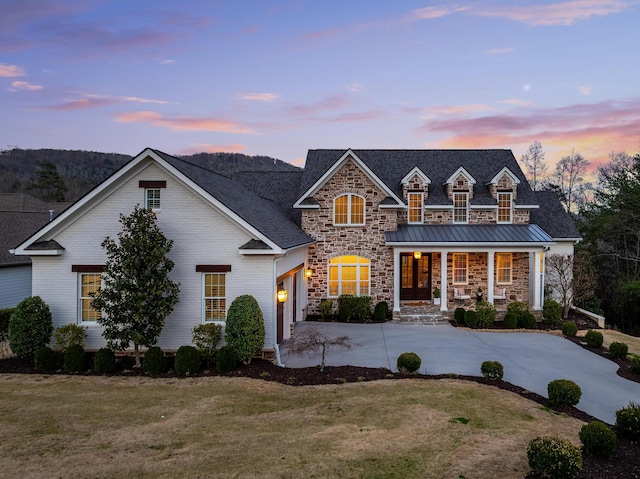 view of front of house featuring a lawn, covered porch, stone siding, driveway, and a standing seam roof