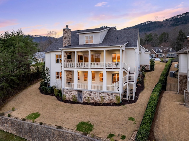 back of house at dusk with central AC, a chimney, a balcony, a mountain view, and a ceiling fan