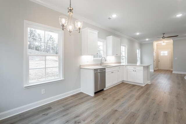 kitchen featuring a peninsula, a sink, light countertops, stainless steel dishwasher, and crown molding