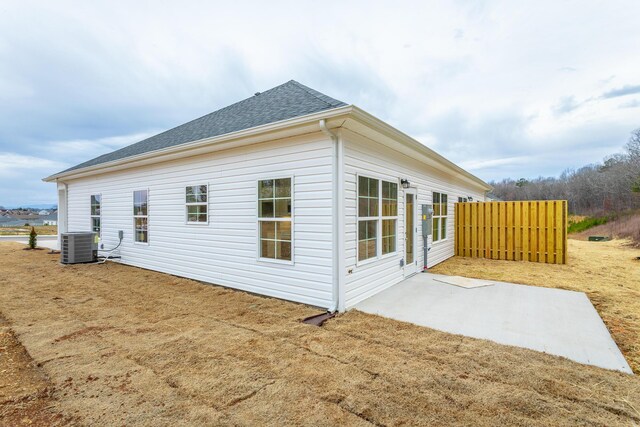 view of property exterior with cooling unit, roof with shingles, a patio, and fence