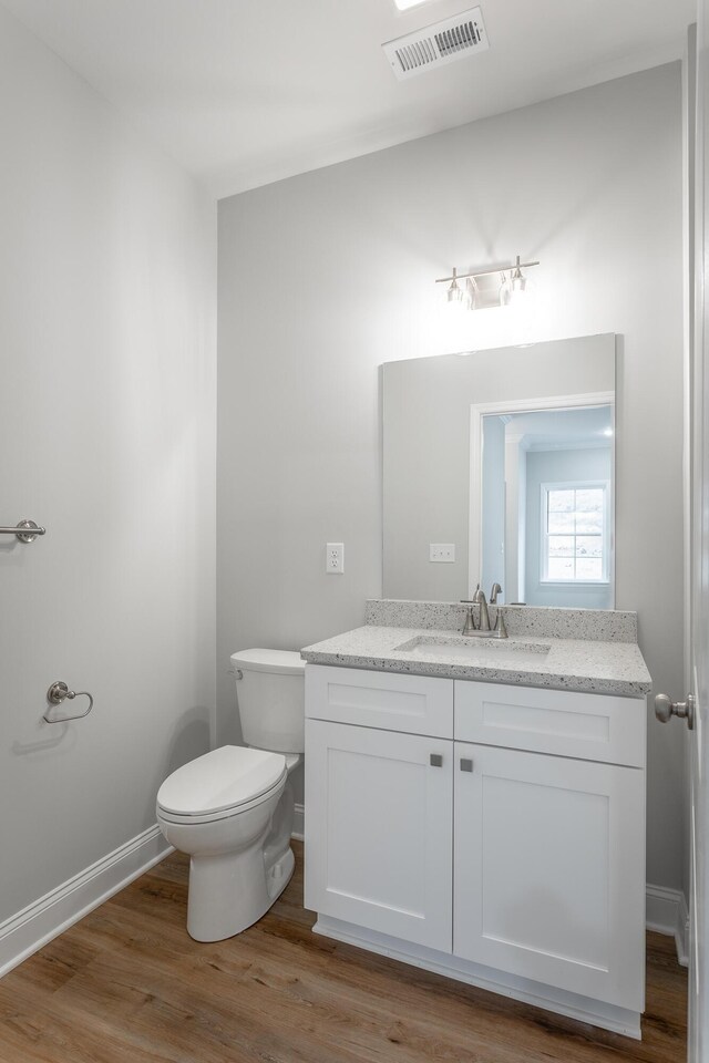 bathroom featuring toilet, wood finished floors, vanity, visible vents, and baseboards