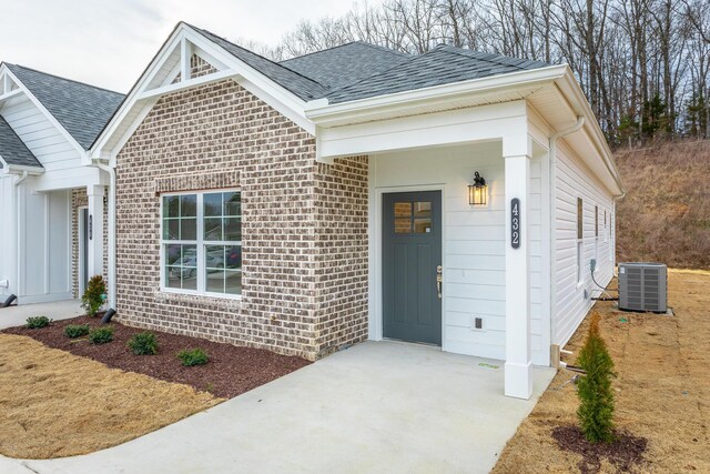 entrance to property with roof with shingles, central AC, and brick siding