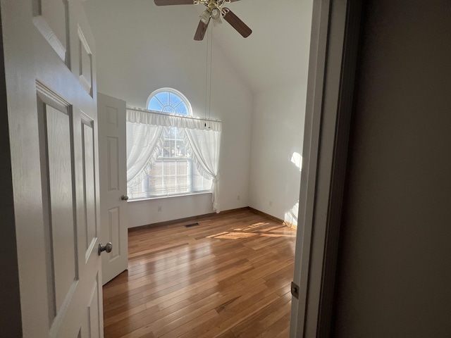 empty room featuring ceiling fan, high vaulted ceiling, hardwood / wood-style flooring, visible vents, and baseboards