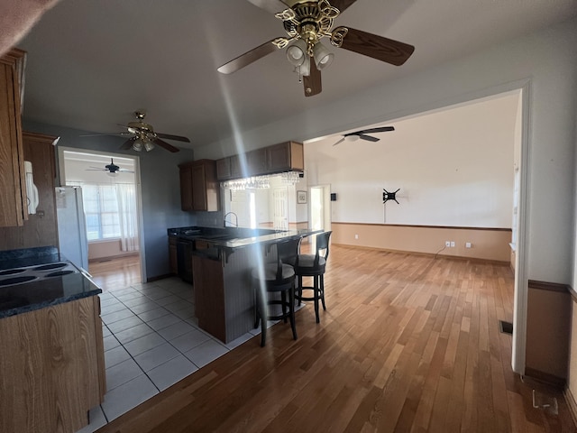 kitchen featuring a breakfast bar, white appliances, dark countertops, and wood finished floors