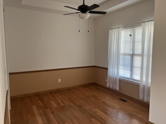 unfurnished room featuring wood-type flooring, visible vents, ceiling fan, and baseboards